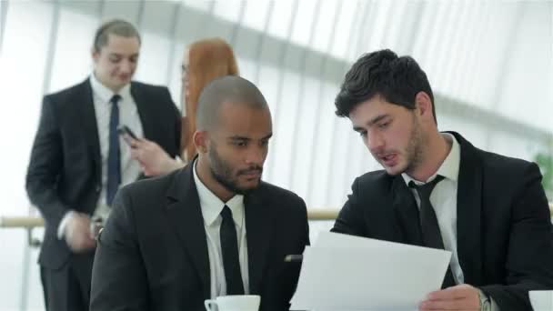 Двоє успішних бізнесменів посміхаються сидячи за столом в офісі — стокове відео