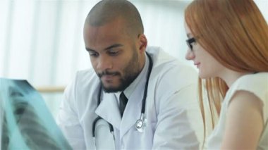 Hastanede bir masada otururken hastayla konuşan gülümseyen doktor