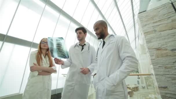 Три уверенных врача, осматривающих рентгеновский снимок легких в больнице — стоковое видео