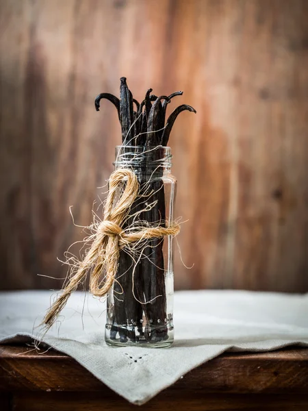 Vanille plakt in een glazen pot op een rustieke houten tafel. — Stockfoto