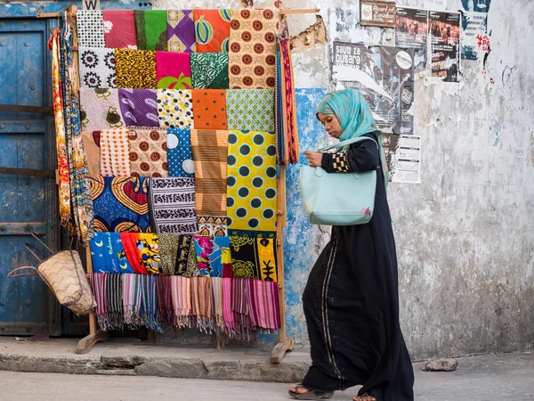 Žena chodí vedle stojanu s barevnými africké oděvy — Stock fotografie