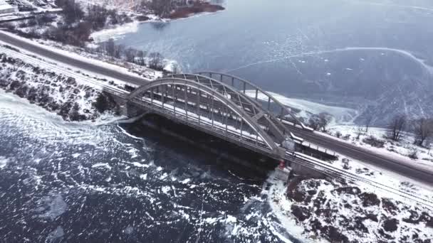 乘坐无人驾驶飞机平稳地飞越一座桥和一条冰冻的河流 汽车沿着大路飞驰而过 冬季来临 寒冷的声调 平稳地向后飞去 带着一个凸起的摄像机 可以看到整个浮桥 — 图库视频影像