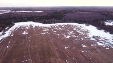 Tarlanın üzerinde, ormanın etrafında, günbatımının arka planında, bahar mevsiminde, bazı yerlerde kar vardır, bulutlu gökyüzü.