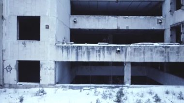 Kameranın pürüzsüz uçuşu, terk edilmiş beton bir bina, boş pencereler ve balkonlar, kamera kapanır, soğuk tonlar