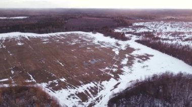 Tarlanın üzerinde, ormanın etrafında, günbatımının arka planında, bahar mevsiminde, bazı yerlerde kar vardır, bulutlu gökyüzü.