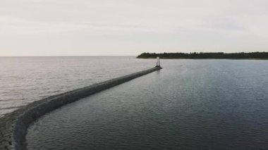 Gölün üzerinden yumuşak bir uçuş, küçük bir deniz fenerine giden uzun taş bir yol, demir bir yapı, beyaz tahta parçaları, ağaçlar yarım güneş, şafak, gökyüzü hafif biraz turuncu, drone üstten görünümü