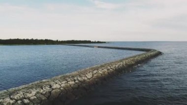 Su üzerinde büyük taşlardan oluşan bir patika, bir göl, uzaktaki bir orman, gökyüzü parlak, mavi, bir dron üzerinde pürüzsüz bir uçuş