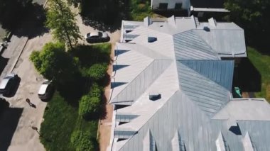 Küçük beton evlerin gri çatıları üzerinde yumuşak bir uçuş, yaz, yeşil ağaçlar, asfalt yollar, bazı yerlerde arabalar var.