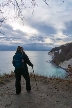 Ruegen Adası 'ndaki Jasmund Ulusal Parkı' ndaki tebeşir kayalıklarından Baltık Denizi 'ne bakan sırt çantalı kadın.