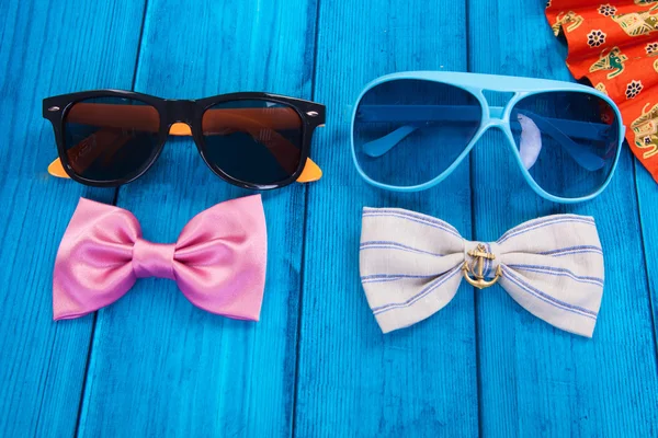 Fan with red bow tie and sunglasses on blue wooden background — Stock Photo, Image