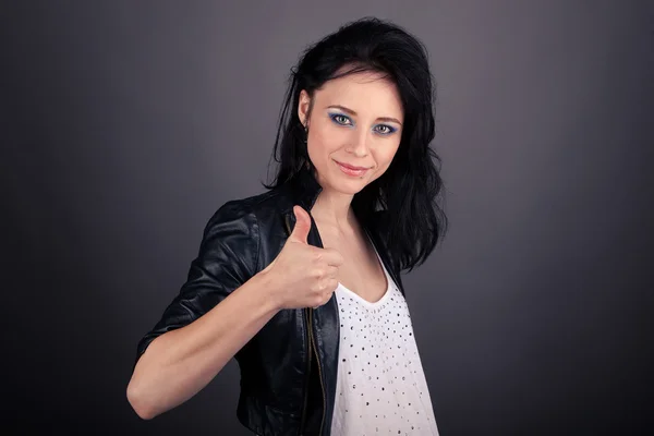 Linda chica en chaqueta de cuero mostrando gestos con sus manos sobre fondo gris — Foto de Stock