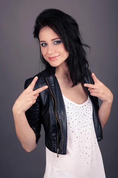 Pretty girl in leather jacket showing gestures with her hands on gray background — Stock Photo, Image