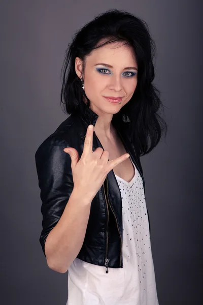 Красива дівчина в шкіряній куртці, що показує жести руками на сірому фоні — стокове фото