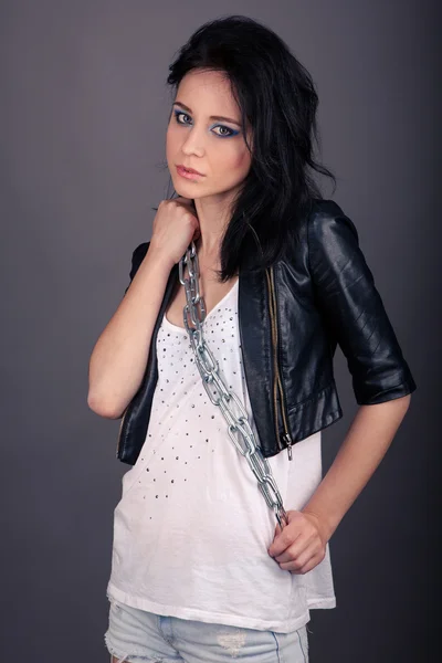 Pretty girl in leather jacket with chains on his hands on a gray background — Stock Photo, Image