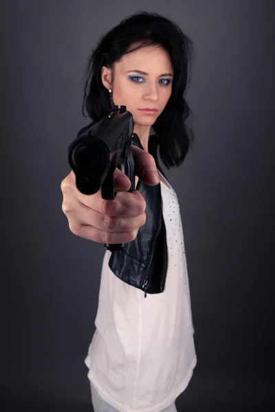Söt flicka i skinnjacka med pistol i händerna på en grå bakgrund — Stockfoto