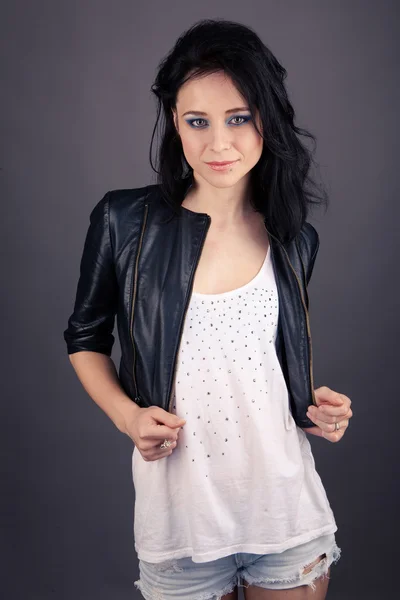 Pretty girl in leather jacket with police handcuffs on a gray background — Stock Photo, Image