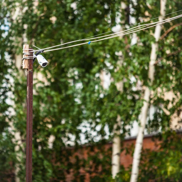 Security camera on the wall of a building with wires on a background of trees — Stock Photo, Image