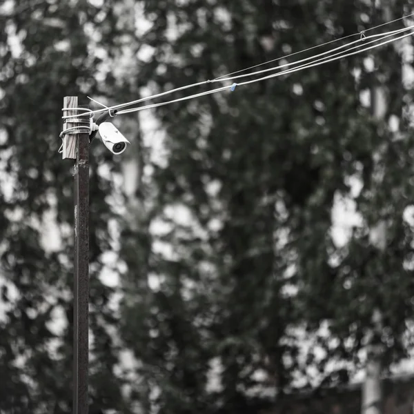 Security camera on the wall of a building with wires on a background of trees — Stock Photo, Image