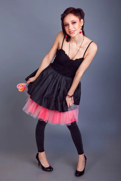 Beautiful girl with short hair licking a lollipop on a gray background — Stock Photo, Image