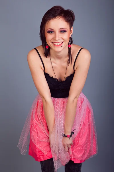 Elegant brunette girl with earrings in pink and black dress on a gray background — Stock Photo, Image