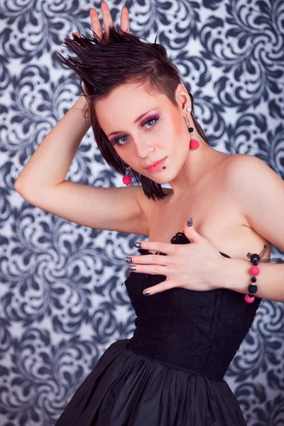Portrait of a beautiful brunette girl with mohawk in red earrings in a black dress on a gray background Stock Photo