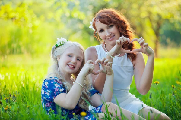 Портрет счастливой матери и маленькой дочери с сердцем в красивом цветущем фруктовом саду с белыми цветами на яблонях — стоковое фото