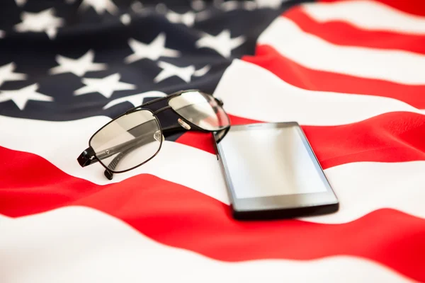 Black smartphone and sunglasses lying on the background of the flag of the United States. — Stock Photo, Image