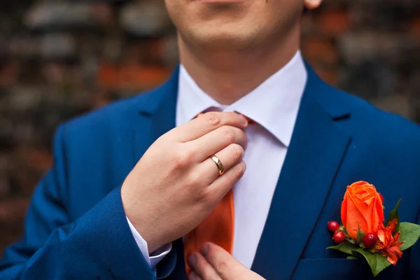 De bruidegom in een blauwe pak past zijn oranje stropdas — Stockfoto