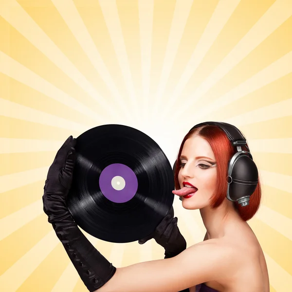 Speelse tong. Kleurrijke foto van een sexy meisje, het dragen van enorme Vintage muziek koptelefoon en likken een paarse LP micro Groove vinyl record op kleurrijke abstracte cartoon stijl achtergrond. — Stockfoto