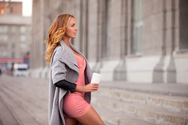 Staden espresso. En vacker kvinna med en kopp kaffe att gå emot stadsbilden. — Stockfoto