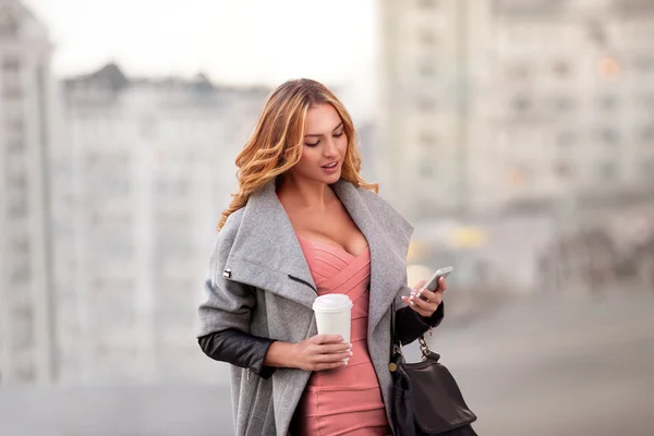 Verksamhet och stil. En affärskvinna inskrivning email via mobiltelefon och håller en kaffekopp mot stadsbilden. — Stockfoto
