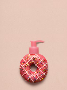 Tatlı ve kremsi. Pembe bir arka plan üzerinde bir kozmetik pompa dispenseri ile lezzetli bir tatlı çilek donut yaratıcı natürmort.