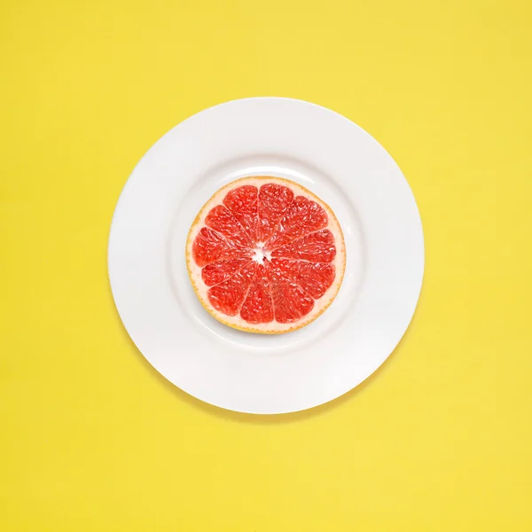 Grapefruit zum Frühstück. rote Grapefruitscheibe auf weißem Teller auf gelbem Hintergrund. — Stockfoto