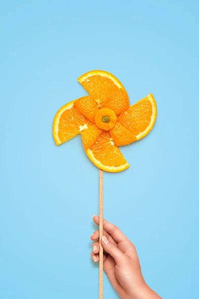 Gyümölcsös szélmalom. Kreatív csendélet egy sárga játék szélmalom készült friss narancssárga szelet kék háttér. — Stock Fotó