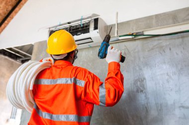 Hastalığı önlemek için maske ve kask takan havalandırma teknisyeni Covid 19 şu anda klima takmak için elektrikli matkap kullanıyor..