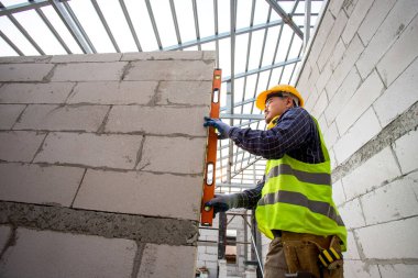 Otoklavize beton bloklarla çalışan duvar inşaatçısını ölçmek için su seviyesi ölçer kullanan bir işçi. İnşaat alanına duvar örme, tuğla yerleştirme.