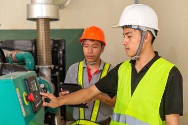 İki Asyalı bakım teknisyeni fabrikadaki su basıncı kontrol sistemi ekipmanlarının teknik verilerini kontrol ediyor.