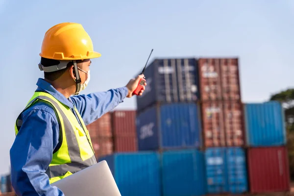 foreman worker wear a mask working use a long distance radio control container cargo harbor to loading containers. Logistics import export shipping concept.