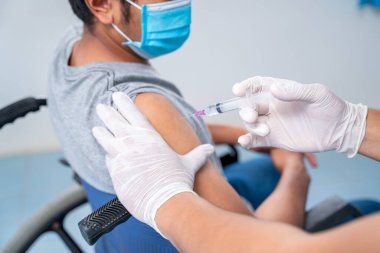 Doktor, engelli kişinin omzuna aşı yapıyor. Koluna grip aşısı, koronavirüs aşısı, covid-19 aşısı, insan klinik denemelerine hazırlanıyor..