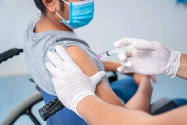 Doktor, engelli kişinin omzuna aşı yapıyor. Koluna grip aşısı, koronavirüs aşısı, covid-19 aşısı, insan klinik denemelerine hazırlanıyor..
