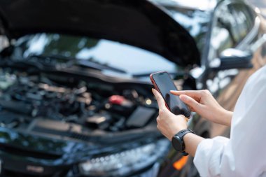 Araba bozulduğu için cep telefonuyla araba tamircisini arayan bir kadının eli kapalı. Araba teknisyeniyle bağlantı kurmak veya yardım konseptine ihtiyaç duymak.