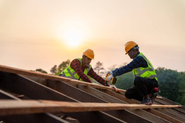 İki Asyalı inşaat işçisi yeni çatı döşeme araçları, çatı çatısında elektrikli matkap, ahşap çatı yapısının yeni çatılarında kullanılan takım çalışması konsepti.