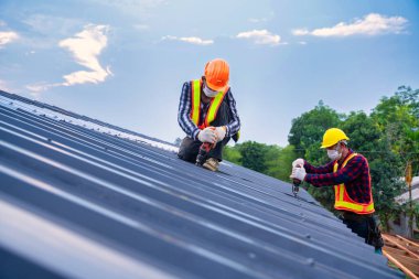Ekip çalışması çatısı konsepti inşaat halindeki konut inşaatı, Roofer işçi güvenlik giyimi hava veya pnömatik çivi tabancası kullanarak ve yeni çatı metal levhası üzerine kurulumu.