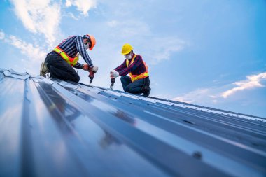 Yeni çatı metal levhası, çatı inşaat konseptine elektrikli matkap aletleri kullanarak çekici işçi güvenliği giysisi.