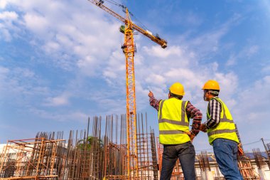 İnşaat mühendisleri ve mimar inşaat projesinin ilerlemesini denetliyor. İnşaat alanındaki yeni beton çatı ve vinç arka planında.