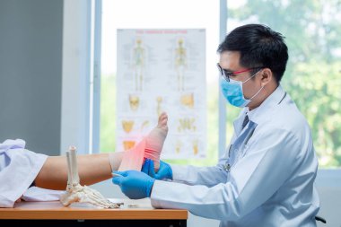 Ortopedi doktoru eldiven takıyor. Klinikte ayak bileği iltihabı olan hastaların başındaki doktoru muayene ediyor..
