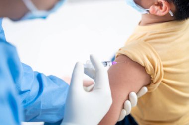 Doktor hasta çocuk ya da çocuğun omzunda aşı yapıyor. Koluna grip aşısı, koronavirüs, covid-19 aşısı aşısı, insan klinik denemelerine hazırlanıyor.