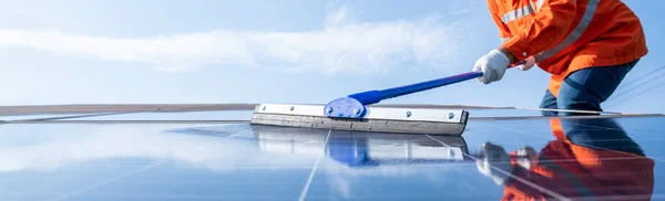 Çalışan teknisyen veya işçilerden oluşan seçici odak paspası, güneş enerjisi santralinin enerji üretmek için bir paspas temizleme güneş paneli kullanır; endüstriyel sektörde iş tanımında endüstri üniforması giyen teknisyen