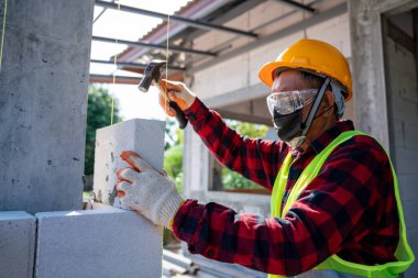 Tuğlacı, otomatik klavuzlu beton bloklar için çekiç kullanıyor. İnşaat alanına duvar örme, tuğla yerleştirme