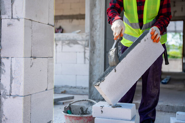 Close up of bricklayer builder using cement mortar to put the Lightweight bricks. at construction site